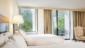 A hotel room with two beds, a lamp, a chair, and a balcony with a table and chairs. - Griffin Hotel, an official Colonial Williamsburg Hotel (Williamsburg)