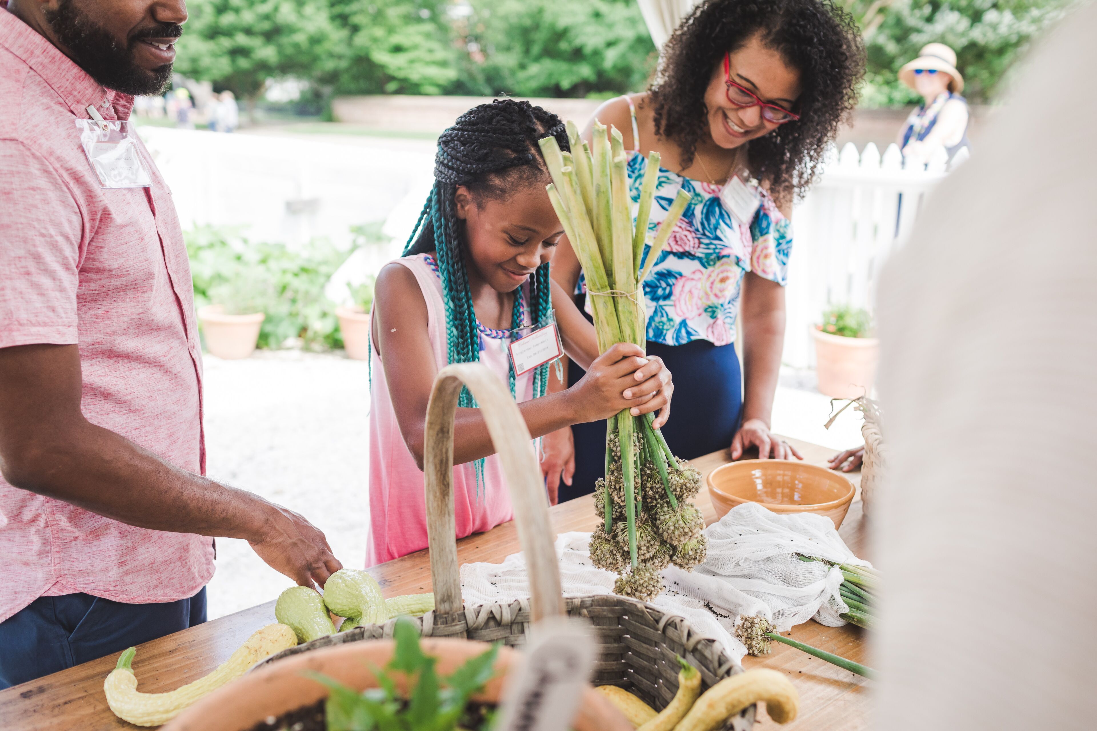 A group of people at a table with fresh vegetables and a basket.