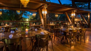 An outdoor dining area with multiple tables and chairs, wooden beams, and hanging light fixtures.