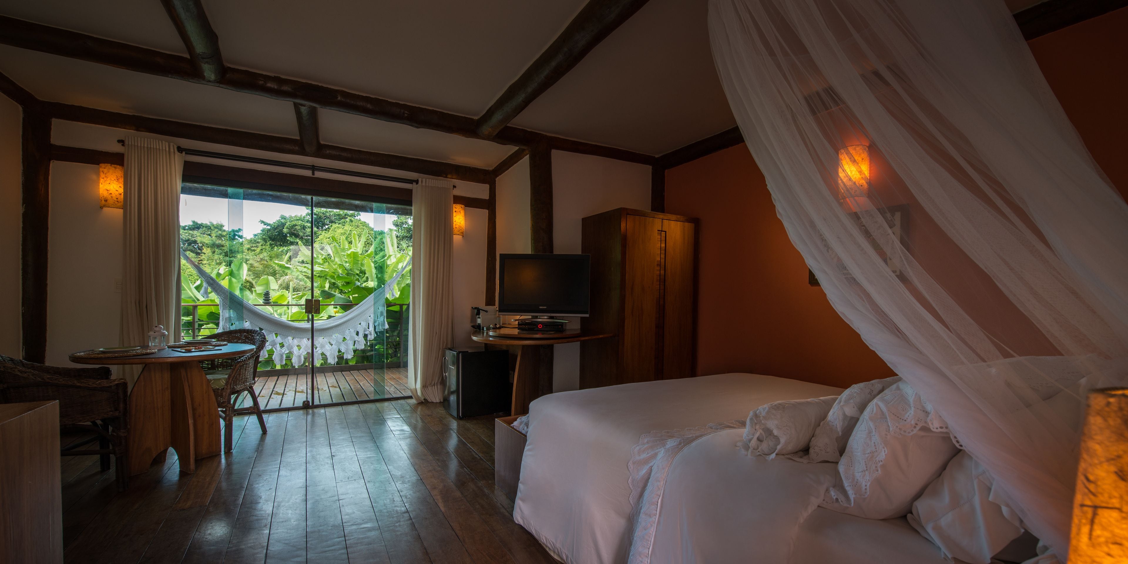 A bedroom with a bed, a TV, a wooden cabinet, a small table, and a hammock.