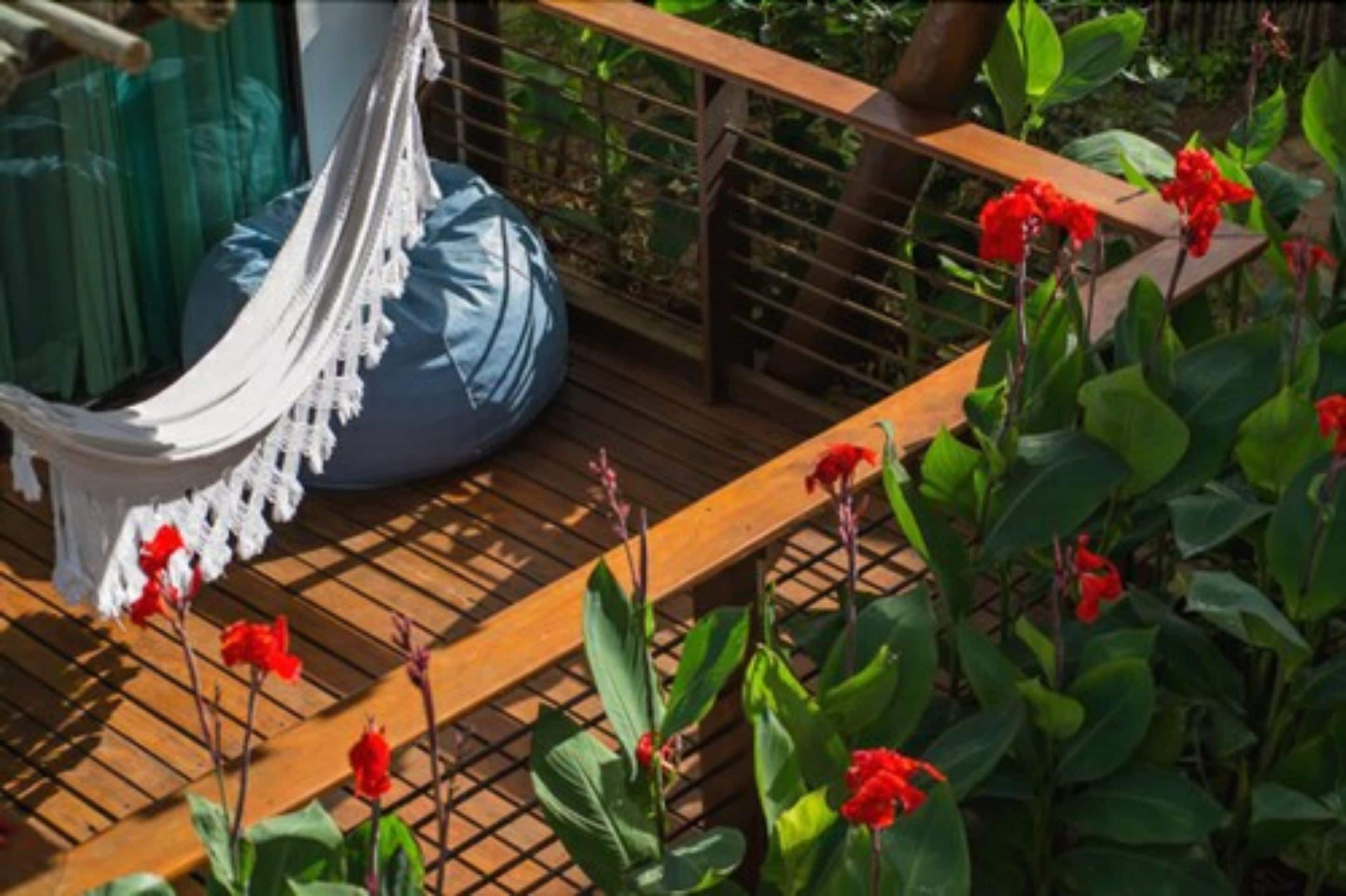 Un hamac sur une terrasse en bois, avec des fleurs rouges en arrière-plan.