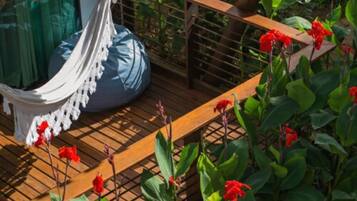 Un hamac sur une terrasse en bois, avec des fleurs rouges en arrière-plan.
