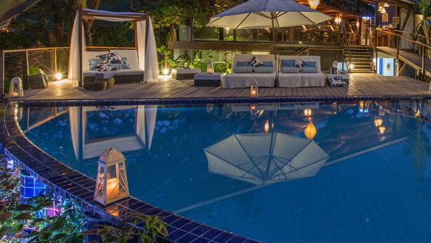 A pool area with a covered seating area, a staircase, and a view of the surrounding greenery.