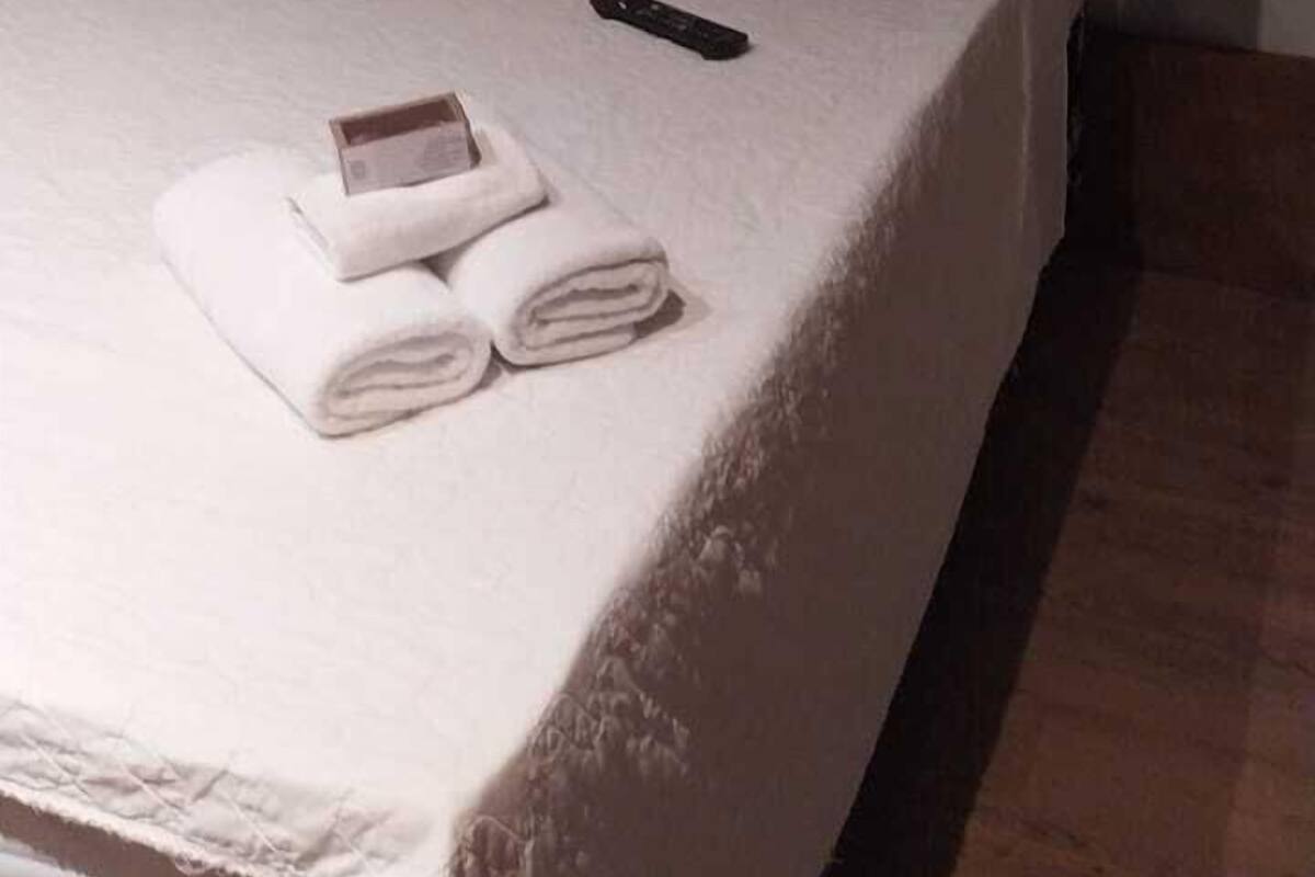 A neatly made bed with a grey tufted headboard, pillows in various colors, a remote control, and rolled towels on the bed.