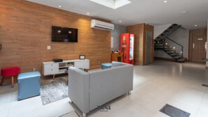 A modern hotel lobby with a wooden wall, a flat-screen TV, a Coca-Cola refrigerator, a staircase, and a sofa. - Plaza Spania (Rio de Janeiro)