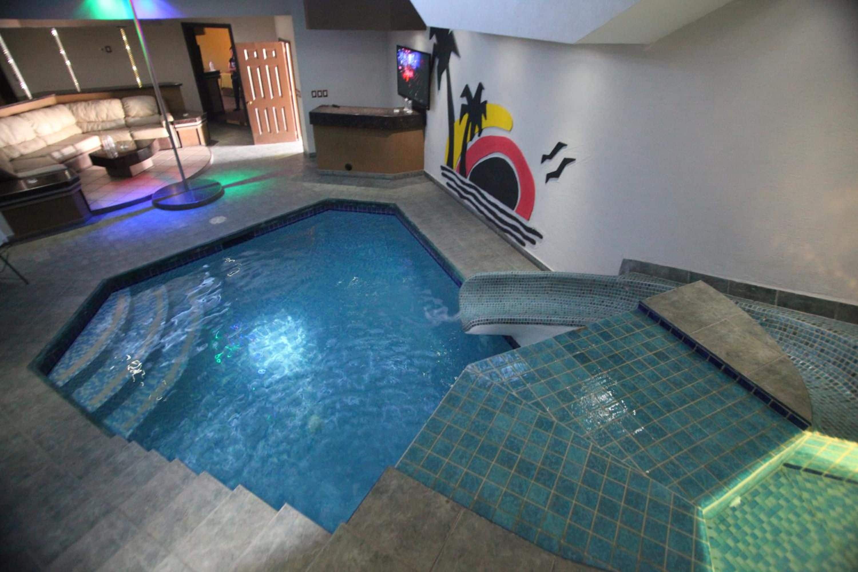 Una piscina interior con solárium de baldosas, un mostrador de recepción y un mural en la pared.