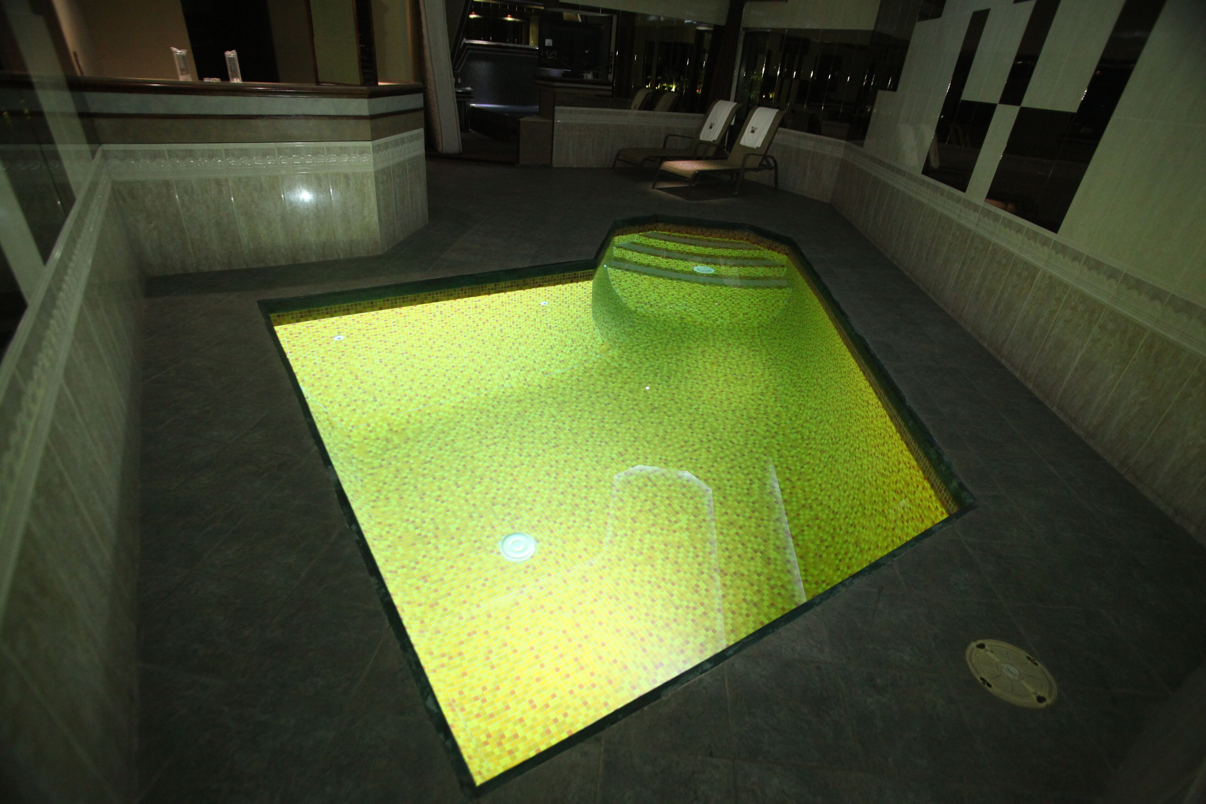 Area piscina con un originale pavimento verde, circondata da posti a sedere e una reception.