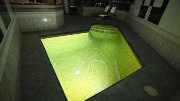 Area piscina con un originale pavimento verde, circondata da posti a sedere e una reception.