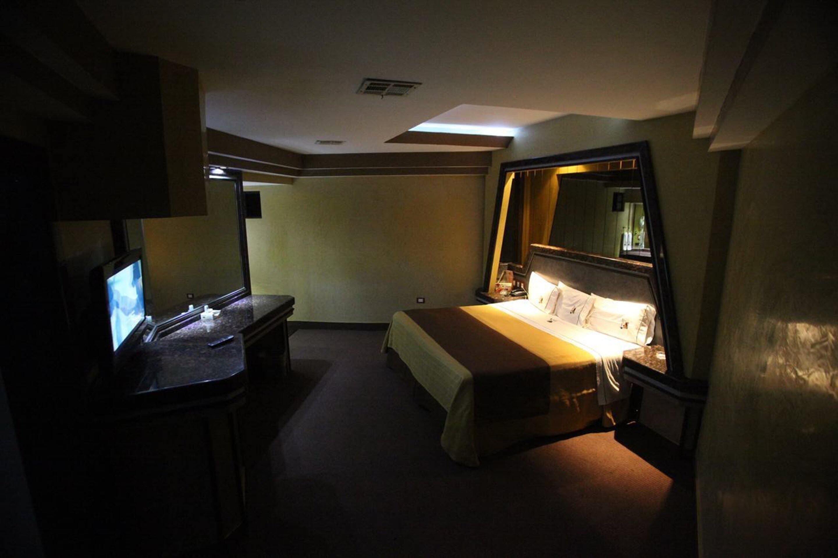 Una habitación de hotel con una cama, un escritorio con ordenador y un espejo grande.