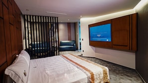 Habitación de hotel con cama, televisor montado en la pared, sofá y un separador decorativo.