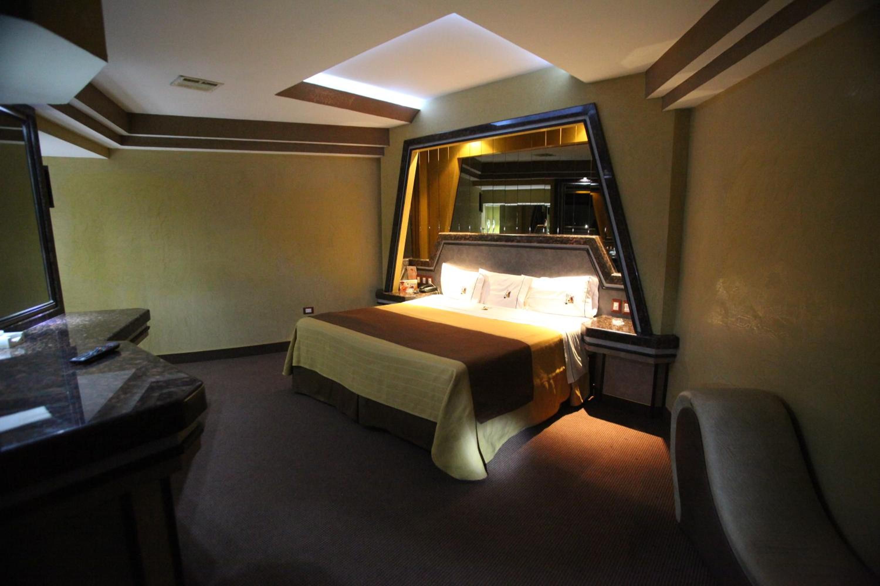 A hotel room with a bed, a desk, a chair, a mirror, and a nightstand.
