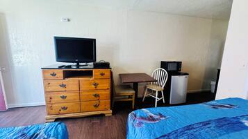 Una habitación con un aparador de madera, un televisor, un microondas, un refrigerador pequeño, una silla y dos camas con ropa de cama azul.