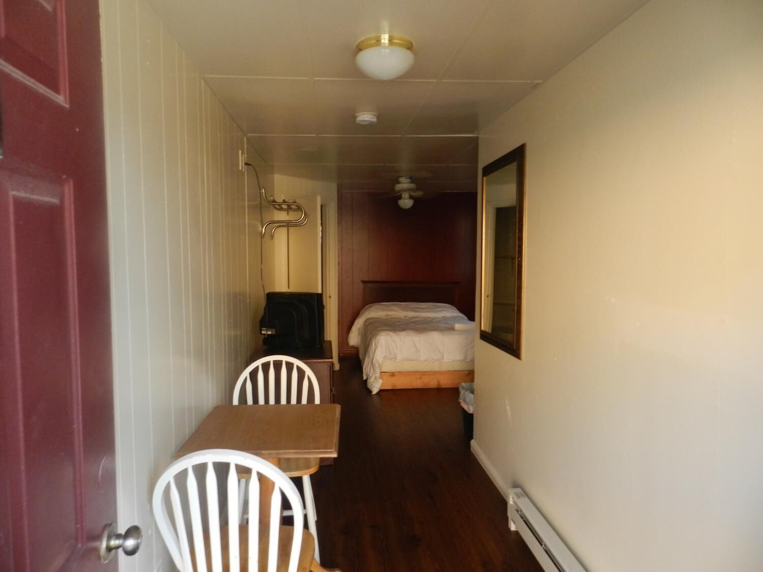 A narrow hallway leading to a bedroom with a bed, a chair, a table, and a coat rack.