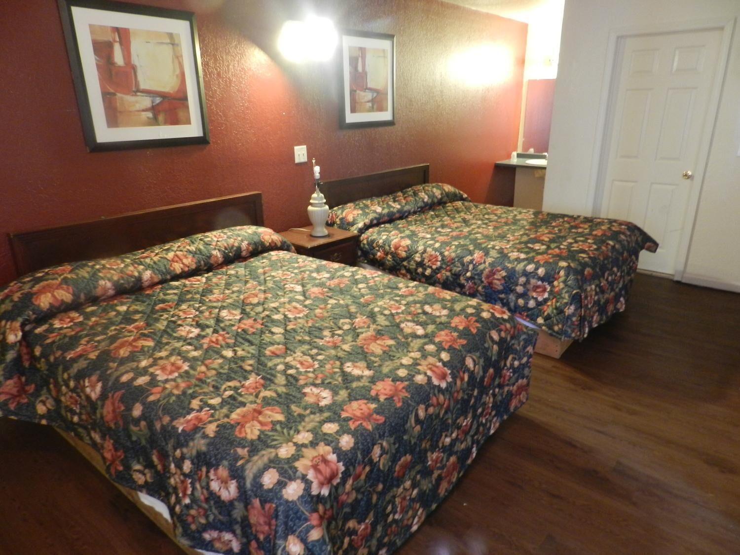 Habitación de hotel con dos camas, ropa de cama estampada, una mesita de noche, una lámpara y cuadros en la pared.