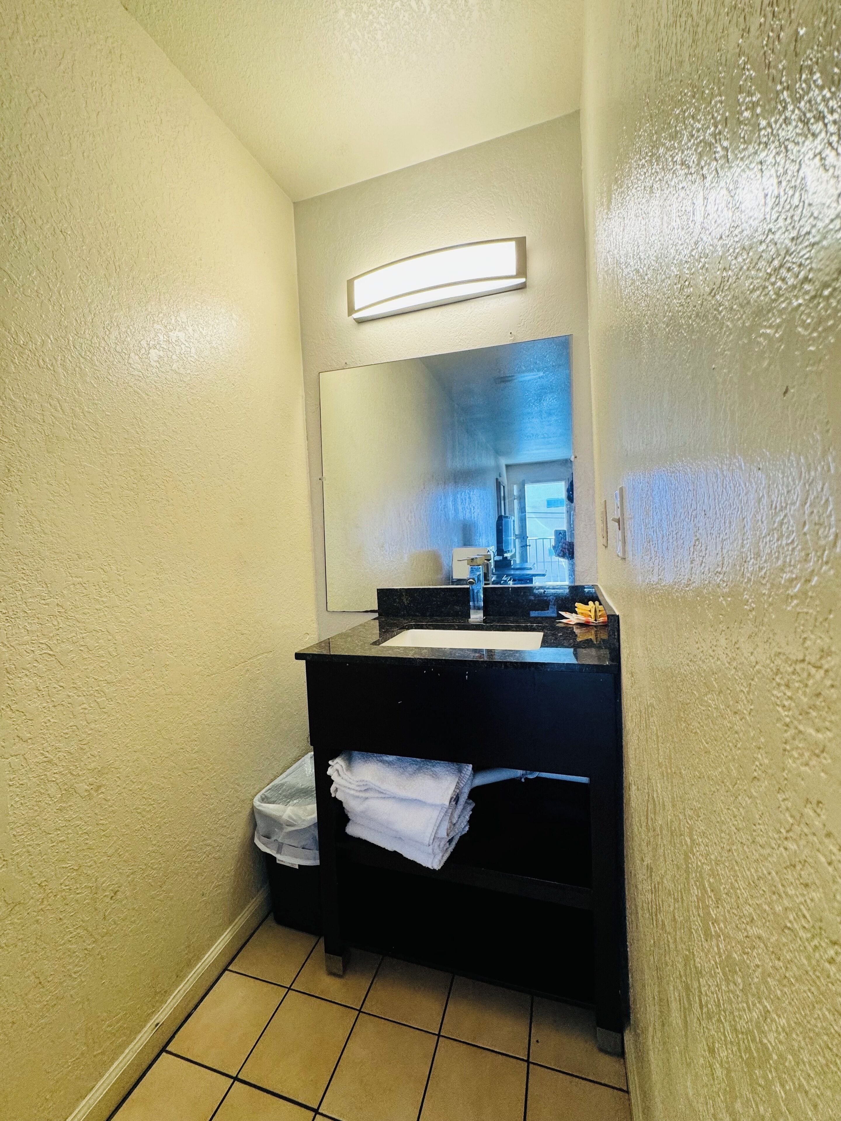 Un baño pequeño con tocador negro, espejo y lavamanos blanco.