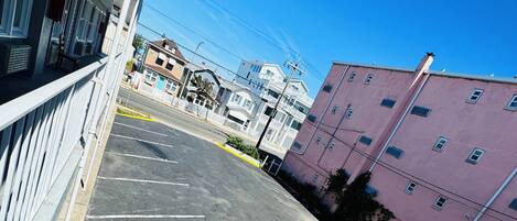 A parking area with marked spaces, a building with a white facade, and a pink building in the background.