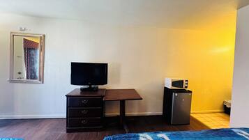 Ein kleiner Raum mit einem Bett, einem Schreibtisch, einem Fernseher, einer Mikrowelle und einem Kühlschrank.