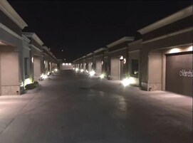 Vista nocturna de un pasillo de hotel con columnas uniformemente distribuidas y letreros iluminados en las paredes.