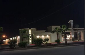 Un hotel moderno con una fachada bien iluminada, una entrada destacada y jardines ajardinados.