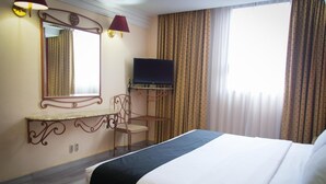 A hotel room with a bed, a television mounted on the wall, a desk with a chair, and curtains on the windows. - Hotel Santa María (Mexico City)