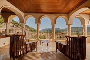 A covered terrace with a tiled floor, wooden furniture, and arched columns. - Cap Vermell Grand Hotel (Capdepera)