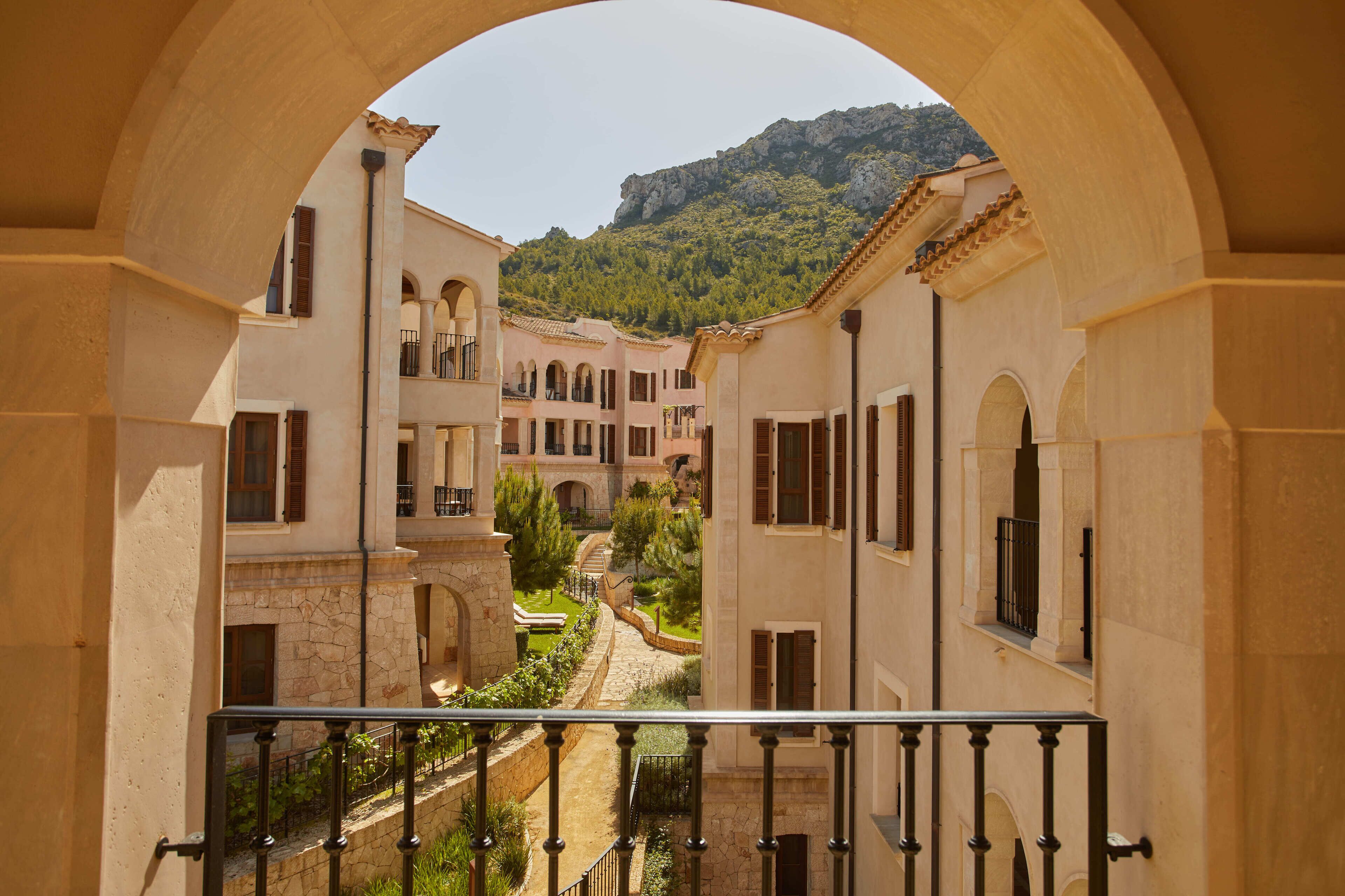 Une cour intérieure avec des allées pavées, des arcades et des bâtiments dotés de balcons et de volets.