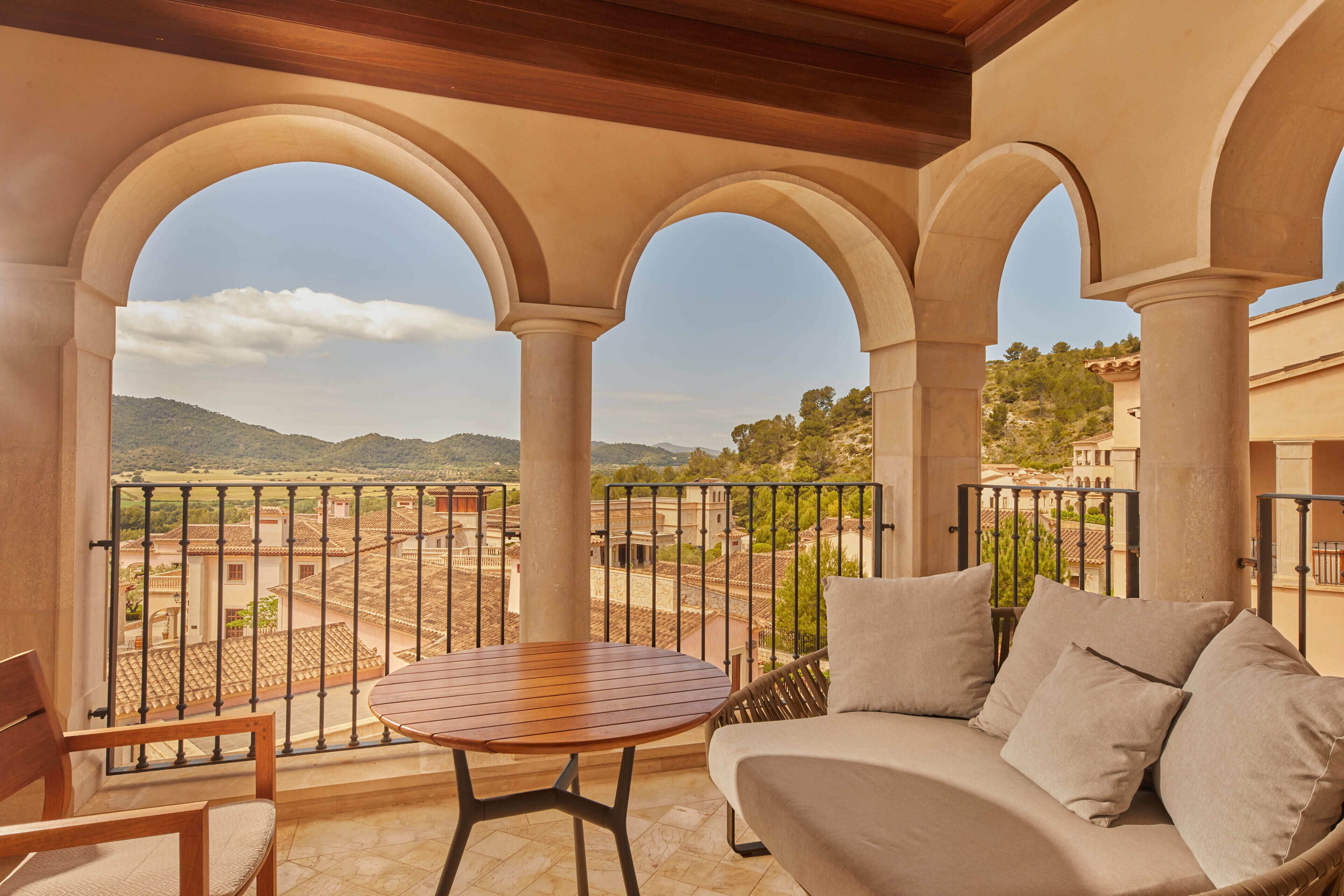 A balcony with a wooden table and a sofa, overlooking a mountainous landscape.