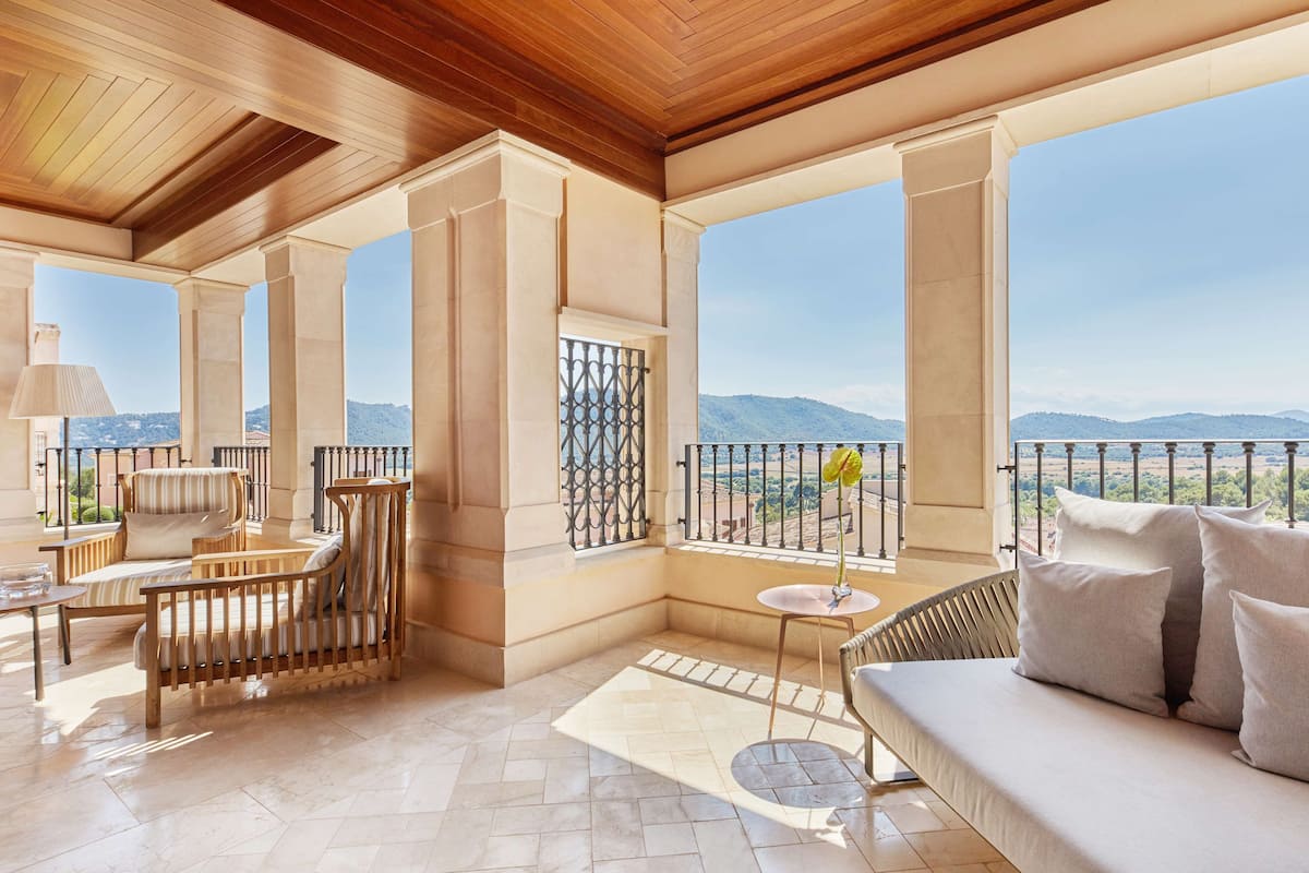 A spacious balcony with a wooden ceiling, a cushioned sofa, a wicker chair, and a small table with a lamp.