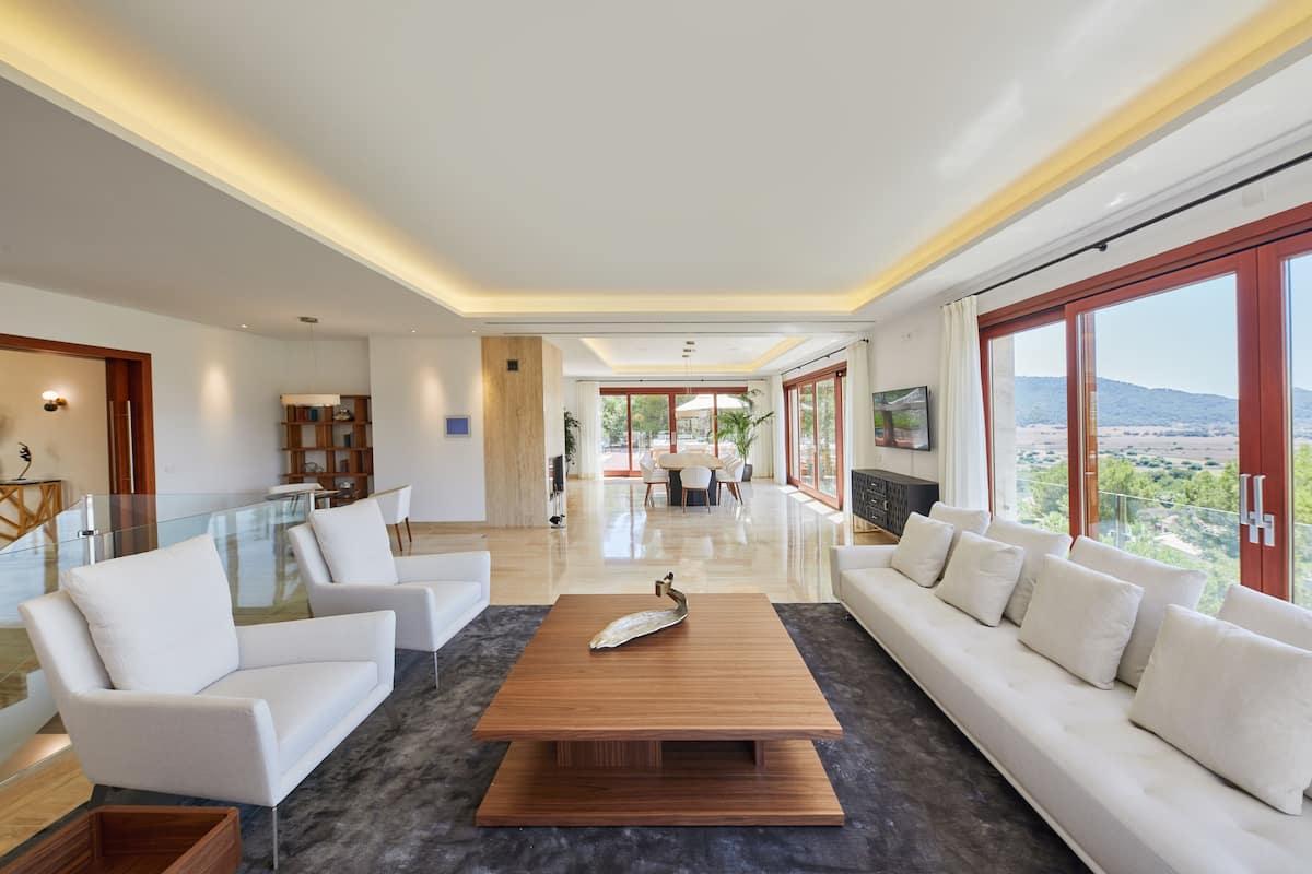 A spacious living room with a wooden coffee table, white sofas, and a glass railing.