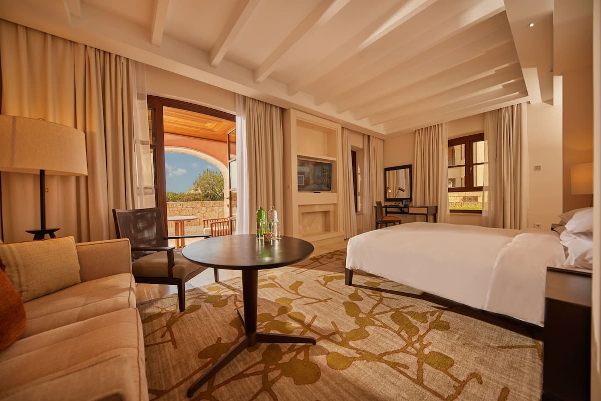 A hotel room with a bed, a sofa, a dining table, and a TV.