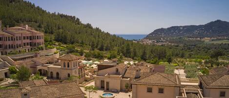 A coastal village with traditional Mediterranean architecture, including terracotta-tiled buildings and a central courtyard with a swimming pool.