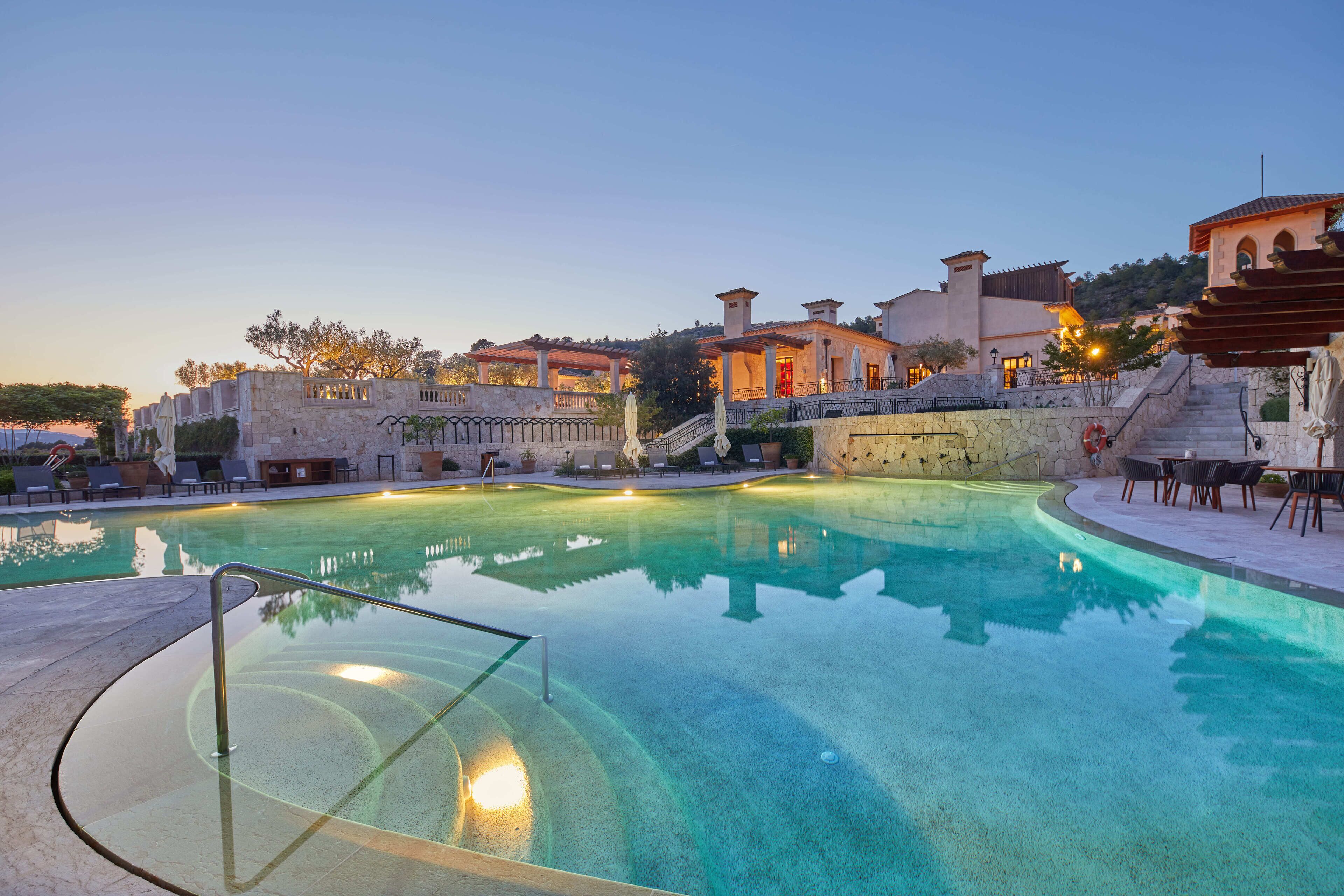 Piscina com guarda-vidro de vidro, paredes de pedra e vista para edifícios ao fundo.
