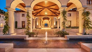 Una entrada imponente con una fuente central, arcos y columnas, que conduce a un edificio con techo de madera e iluminación cálida.