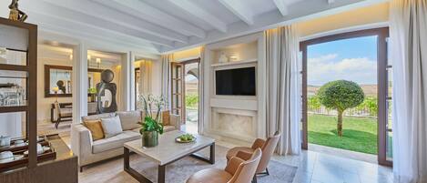Una sala de estar moderna con sofá, mesa de centro y sillas, un televisor de pantalla plana y un ventanal con vistas a un jardín.
