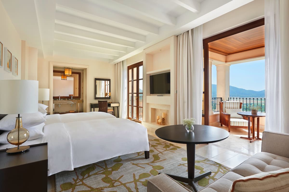A hotel room with a bed, a desk, a TV, a balcony with a view of the mountains.