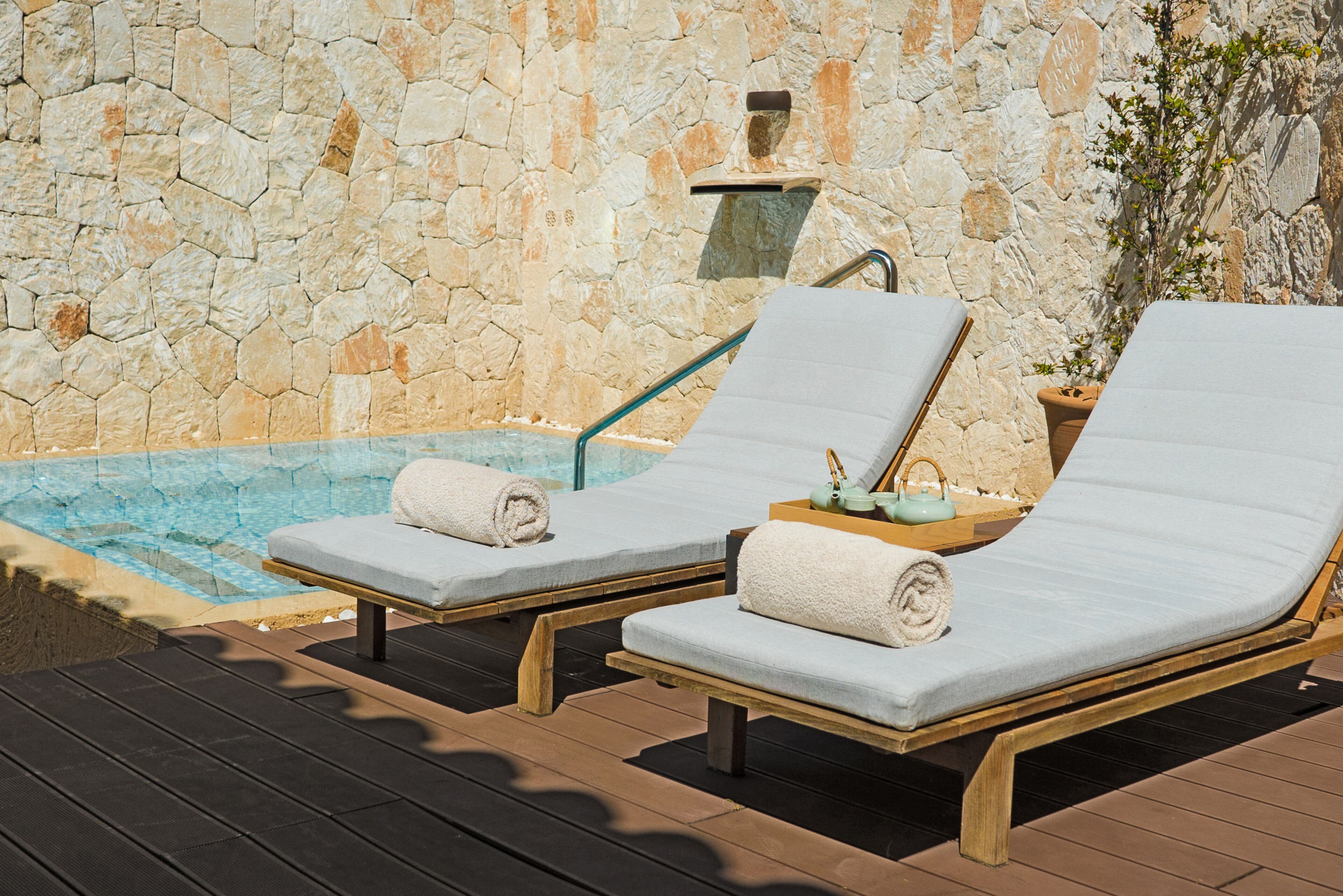 Two sun loungers with towels, a stone wall, and a small pool.