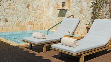 Two sun loungers with towels, a stone wall, and a small pool.