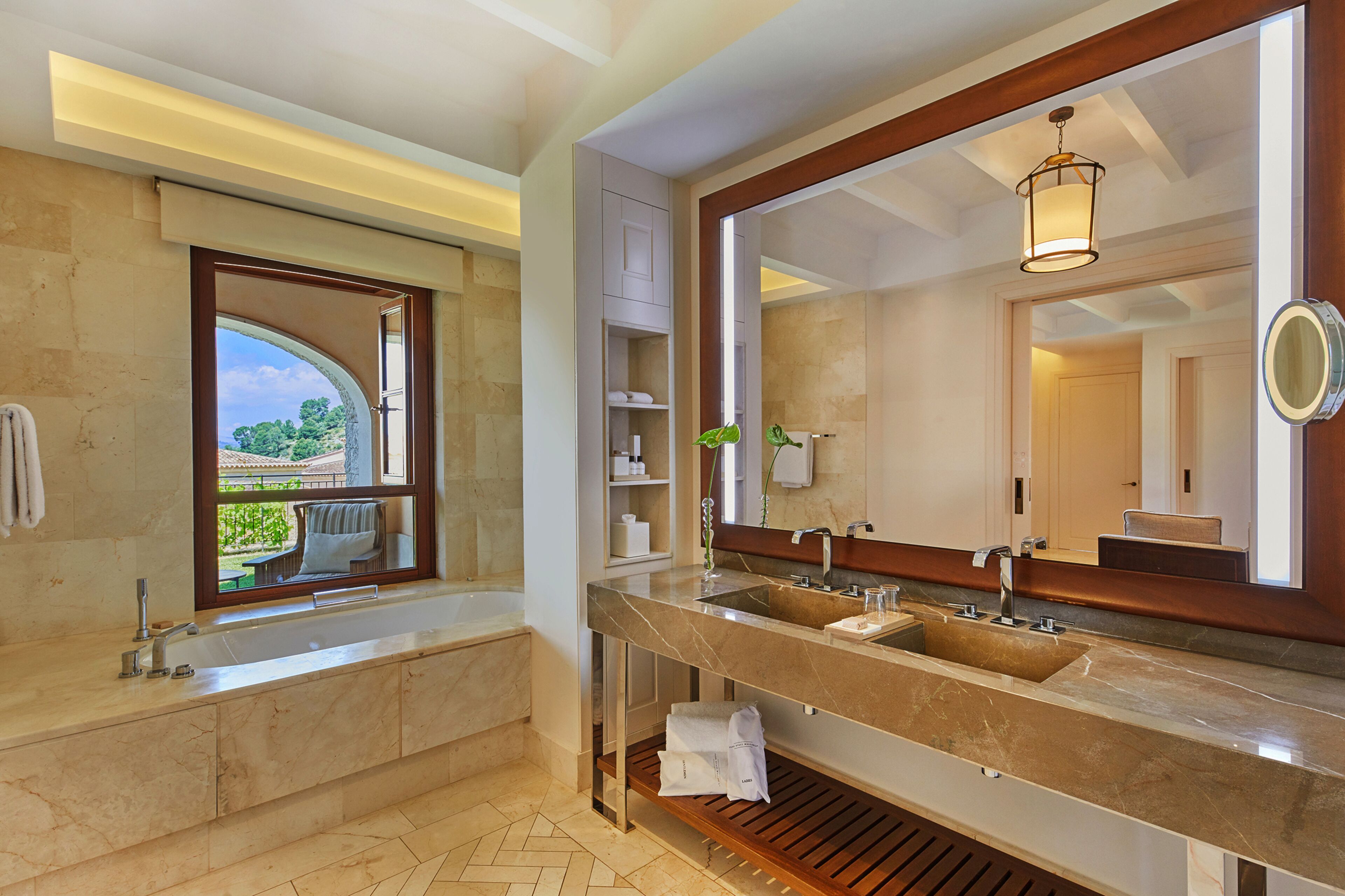 A modern bathroom with a large vanity, dual sinks, a large mirror, and a window offering a view of the outdoors.