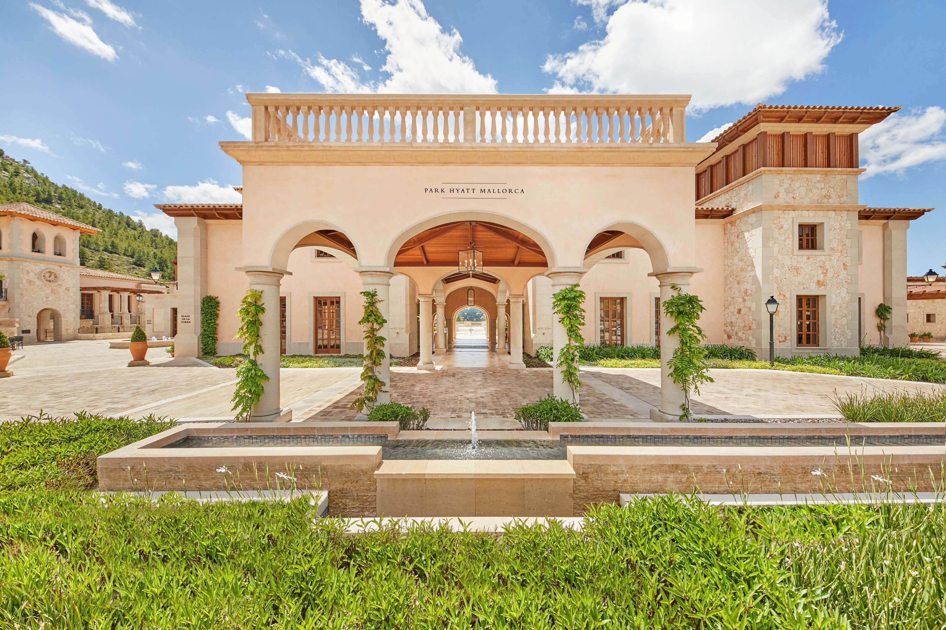 A grand hotel entrance with a central archway, columns, and a fountain.