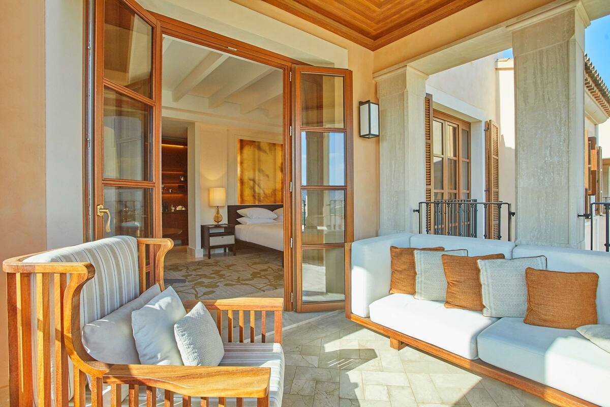A spacious living area with a wooden sofa, a white couch with cushions, and a wooden coffee table.