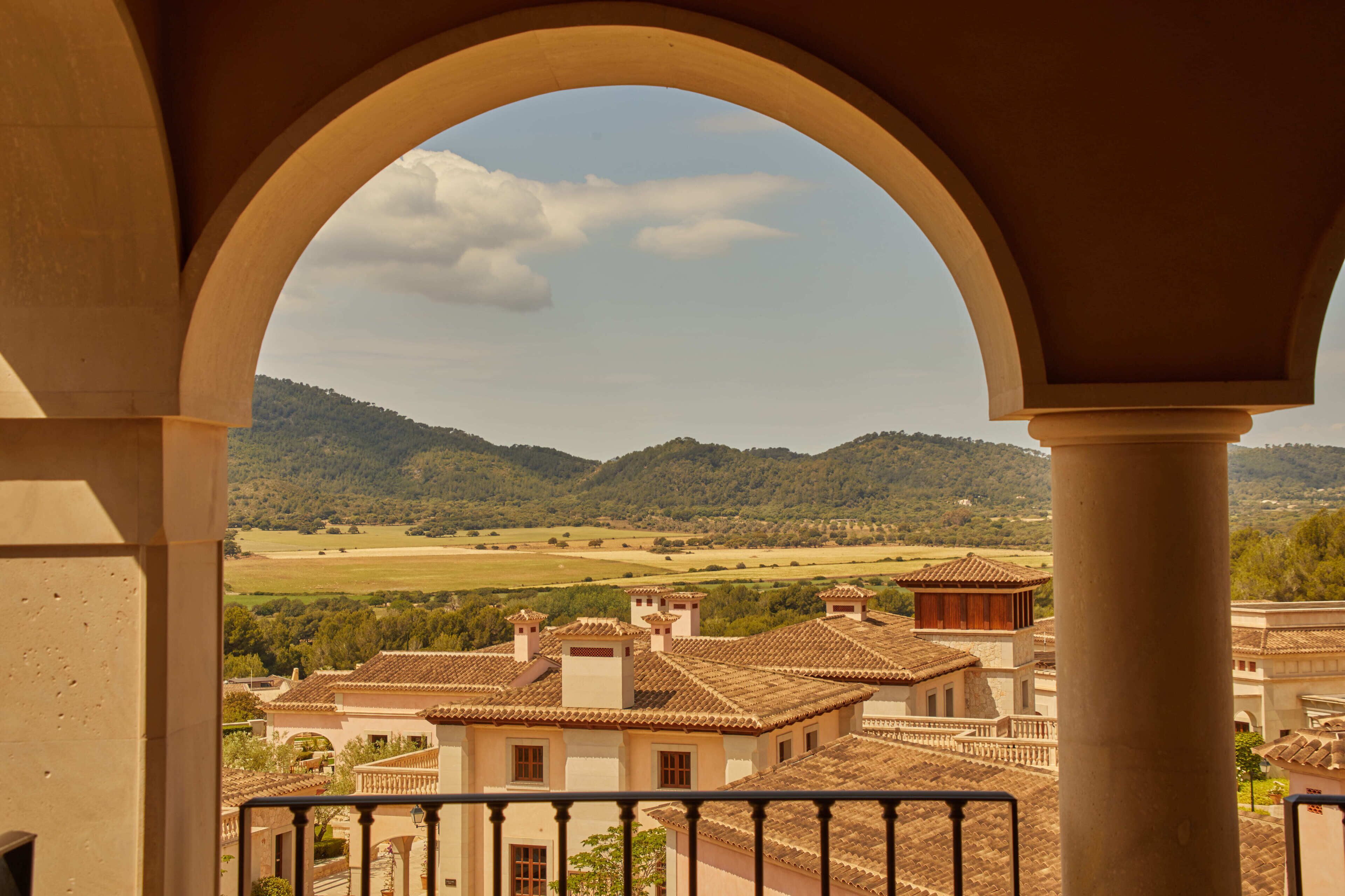 A view through an archway of a residential area with buildings, a hilly landscape, and a clear sky.