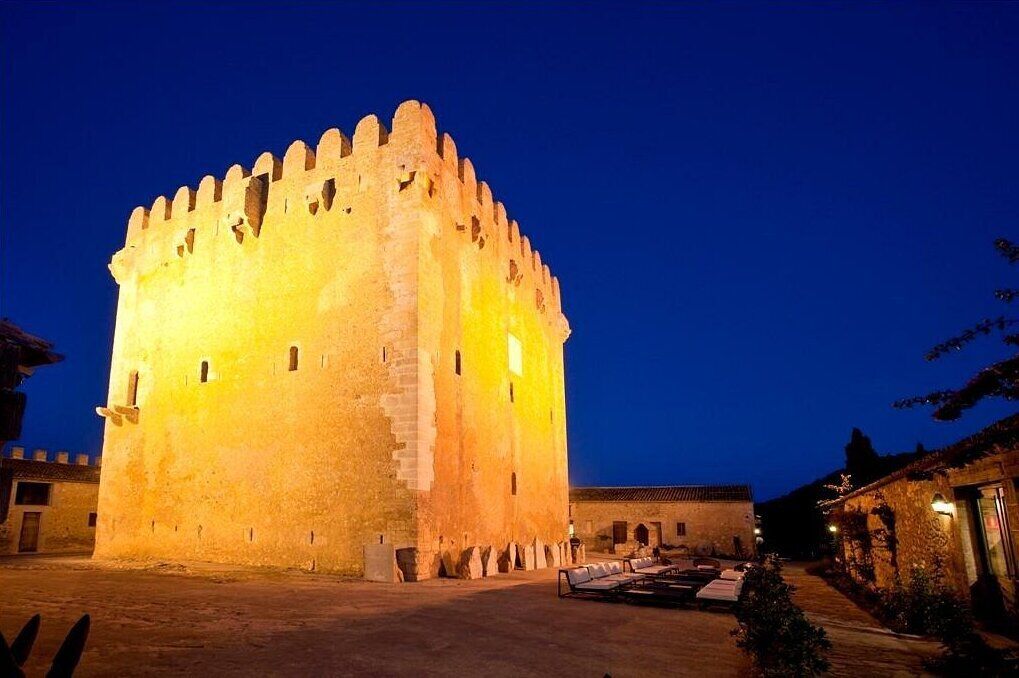 A large, illuminated castle-like structure with a courtyard and a building adjacent to it.