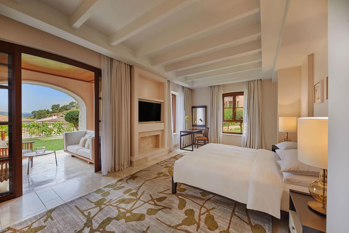 A hotel room with a large bed, a TV, a desk with a chair, and a view of the outdoors.