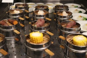 A food display with various dishes in metal containers, some with corn cobs. - Mianyang Fulin Taohuadao Hotel (Mianyang)