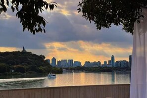 A river with a boat, a city skyline in the background, and a wooden deck. - Mianyang Fulin Taohuadao Hotel (Mianyang)