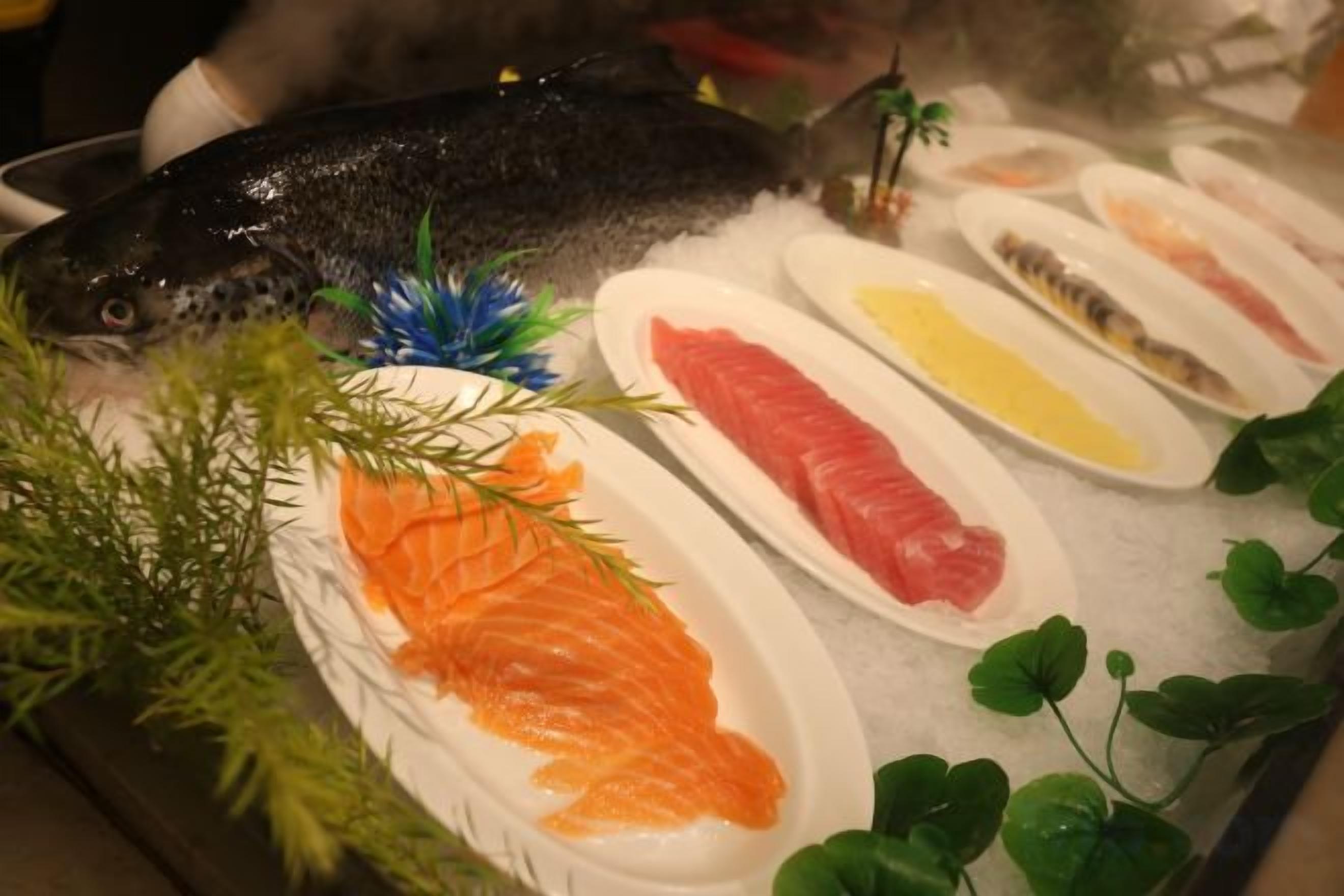 Variedad de mariscos frescos sobre hielo, incluyendo salmón y otros pescados, con adornos de follaje.