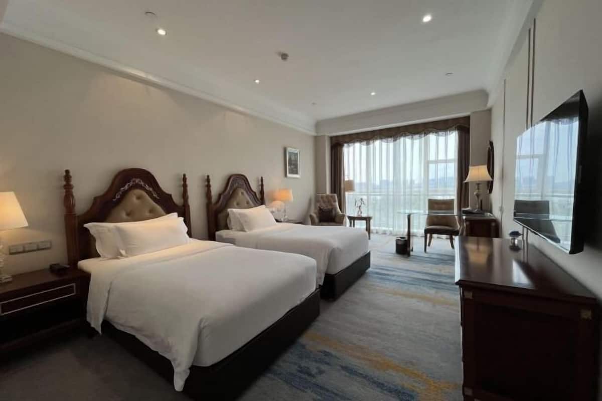 Ein Hotelzimmer mit zwei Betten, einem Fernseher, einem Schreibtisch und Blick ins Freie.