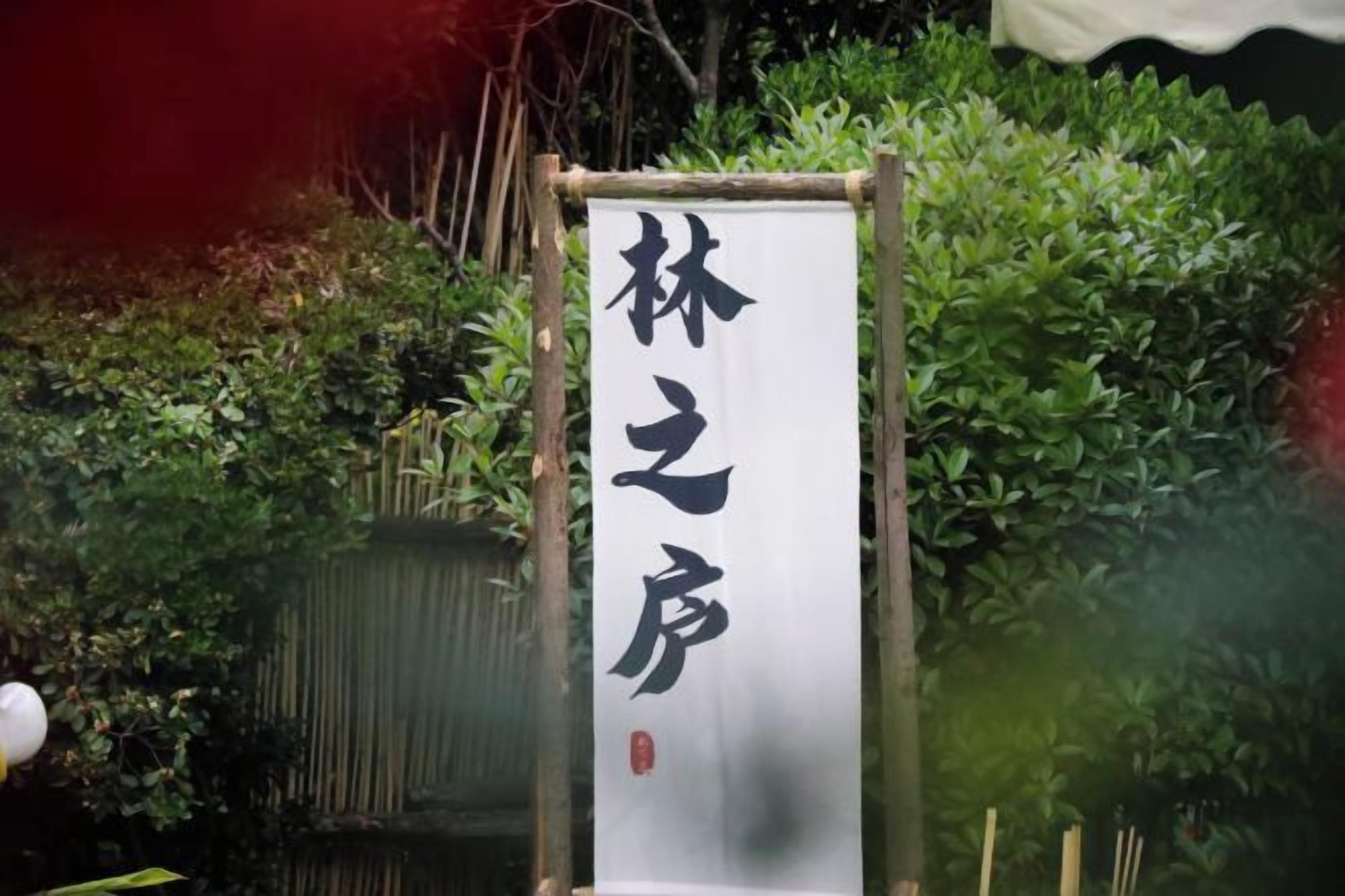A vertical sign with Chinese characters, mounted on a wooden frame, set against a backdrop of dense foliage.