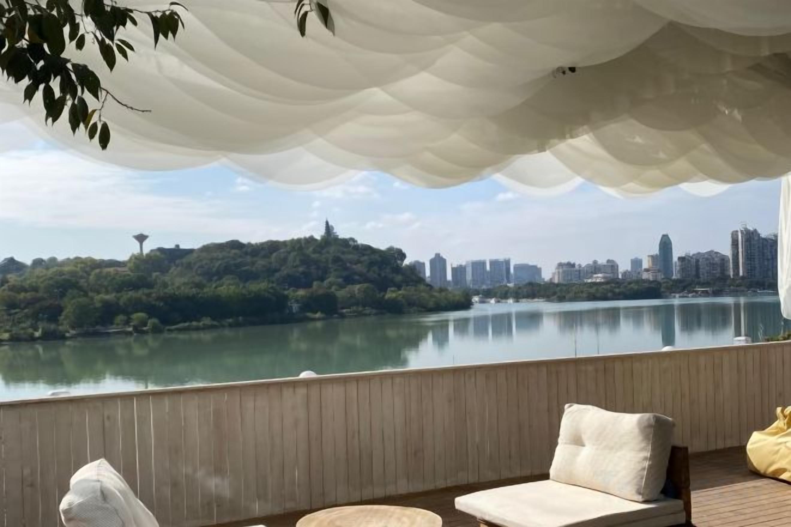 A balcony with a view of a lake and city skyline, wooden flooring, and a white canopy.