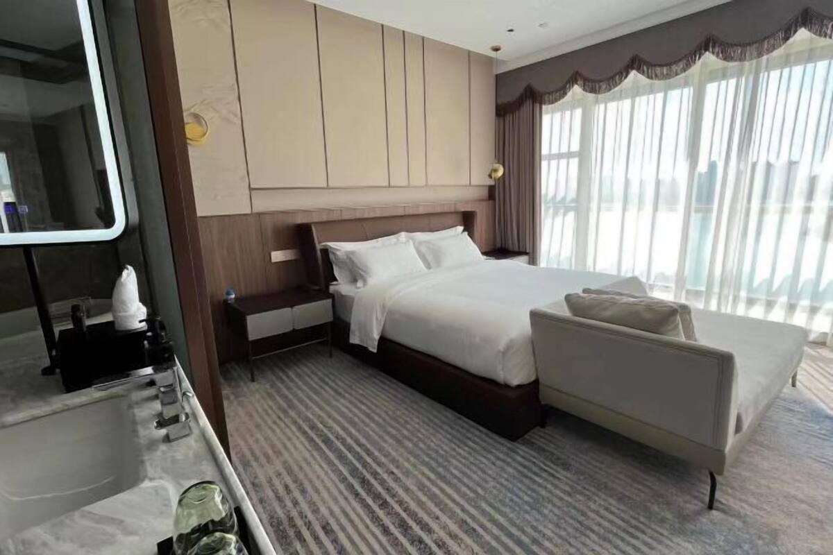 Ein Hotelzimmer mit einem Bett, einer Couch, einem Schminktisch mit Spiegel und einem Fenster mit Vorhängen.